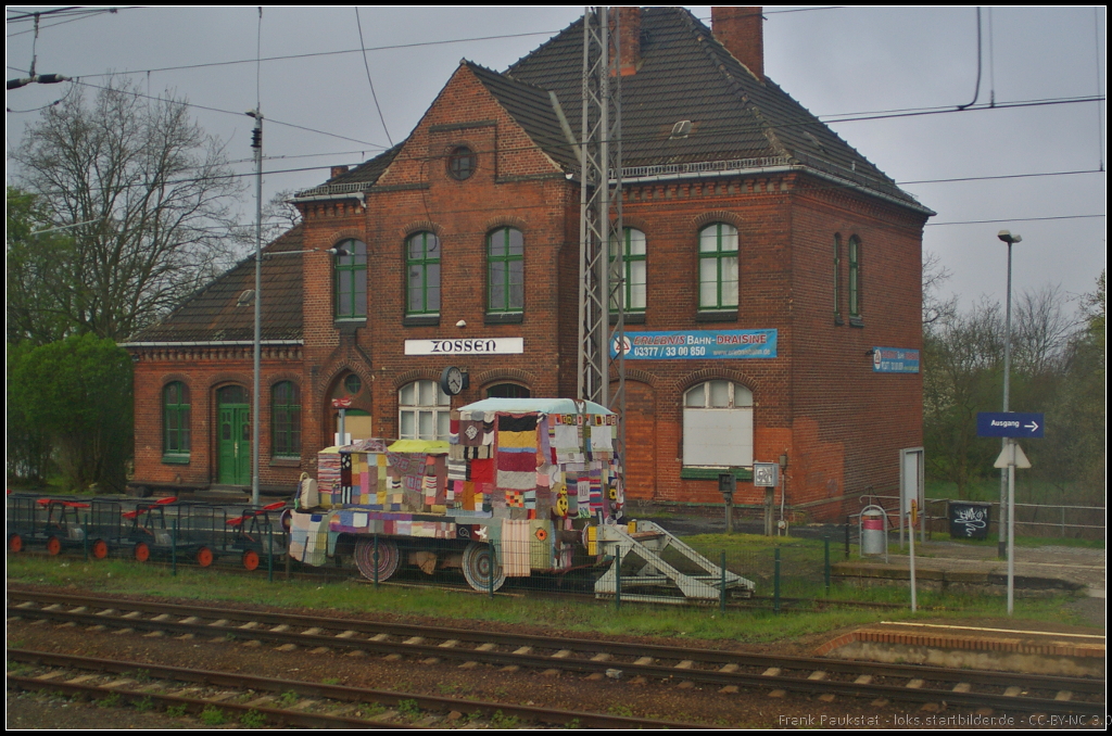 Die bunte Lok f�llt am ehemaligen Bahnhofsgeb�ude von Zossen sofort auf. Hierbei handelt es sich um das Projekt  Stricken f�r den Frieden . Durch die Bestrickung der zweiachsigen Diesellok vom Typ V10 B des ehemaligen DDR-Kraftfuttermischwerks Teltow wollte man so die friedliche Nutzung der ehemaligen K�niglich Preu�ische Milit�reisenbahn hervorheben. Aus dem RE3 in Zossen am 12.04.2014 fotografiert